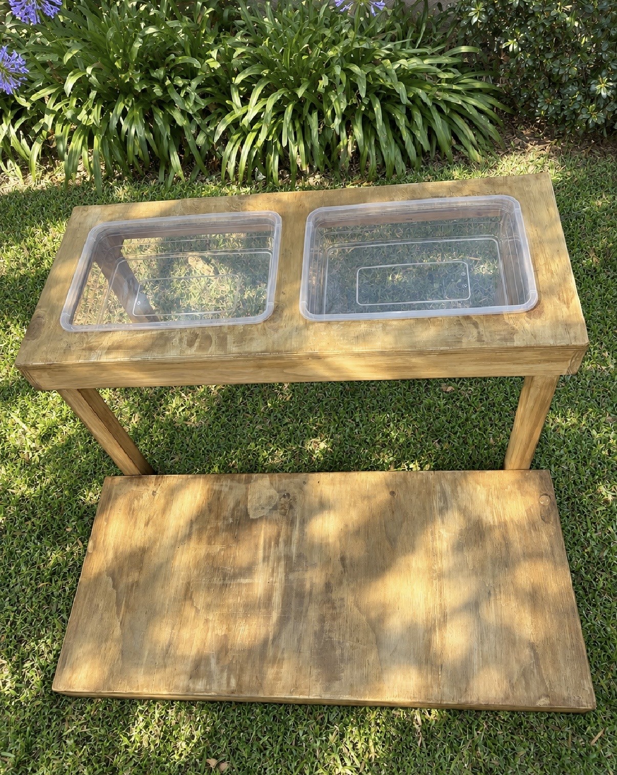 Wooden sensory table with two clear inset tubs in a garden
